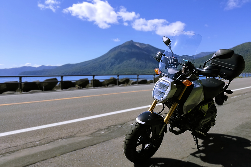 原付バイクの後ろに山と湖の風景が広がる画像