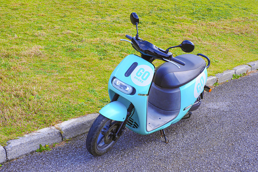公園に駐車されてる、水色の電動バイクの画像