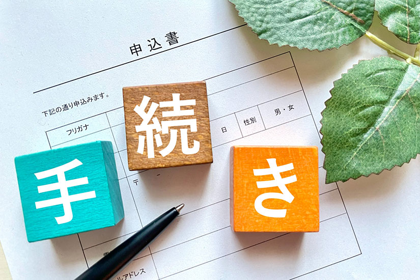 手続きと書かれた木のオブジェと申込書やペン、葉っぱなどが写っている。